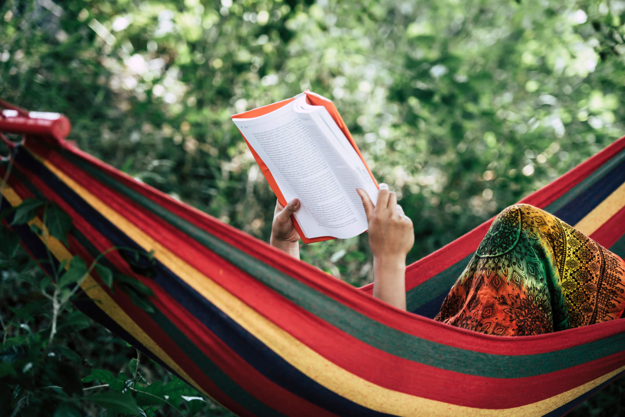 Young woman reading a book lying in a hammock